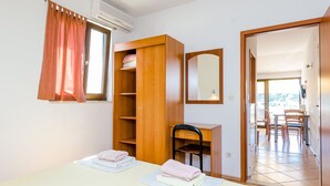 Une pièce comprenant un lit, un bureau, une chaise, une armoire et une salle de bain visible à travers une porte ouverte.