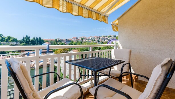 Un balcon avec une table et des chaises, donnant sur un paysage urbain avec des immeubles et des arbres.