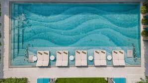 A large rectangular pool with a wavy pattern on the bottom. There are multiple white lounge chairs with green cushions aligned along the pool's edge.