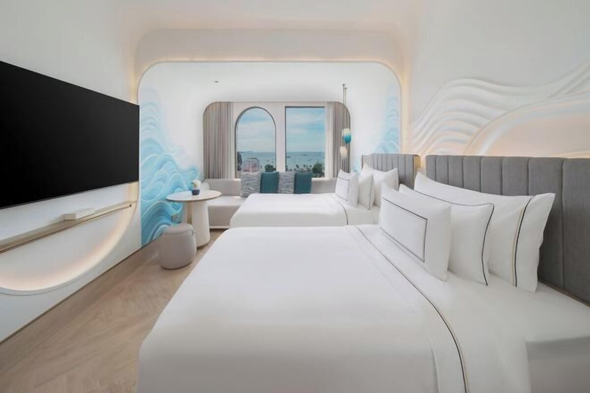 A modern hotel room with a large bed, a TV, and a seating area with a view of the sea.