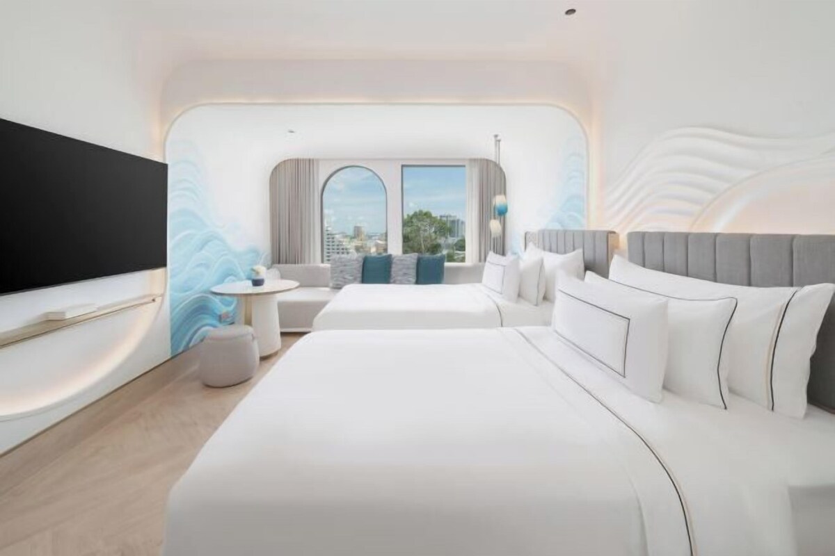 A modern hotel room with a large bed, a seating area with a small table, and a TV mounted on the wall.