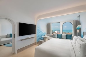 Habitació d'hotel moderna amb un llit gran, televisió de pantalla plana, un sofà i vista al mar.