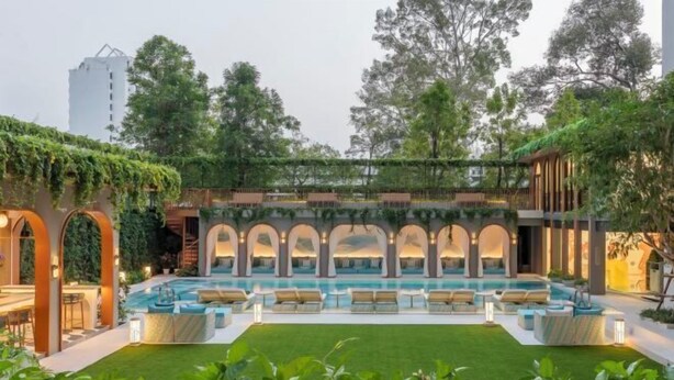 A pool area with multiple lounge chairs and a small pool, surrounded by greenery and a covered seating area with arches.