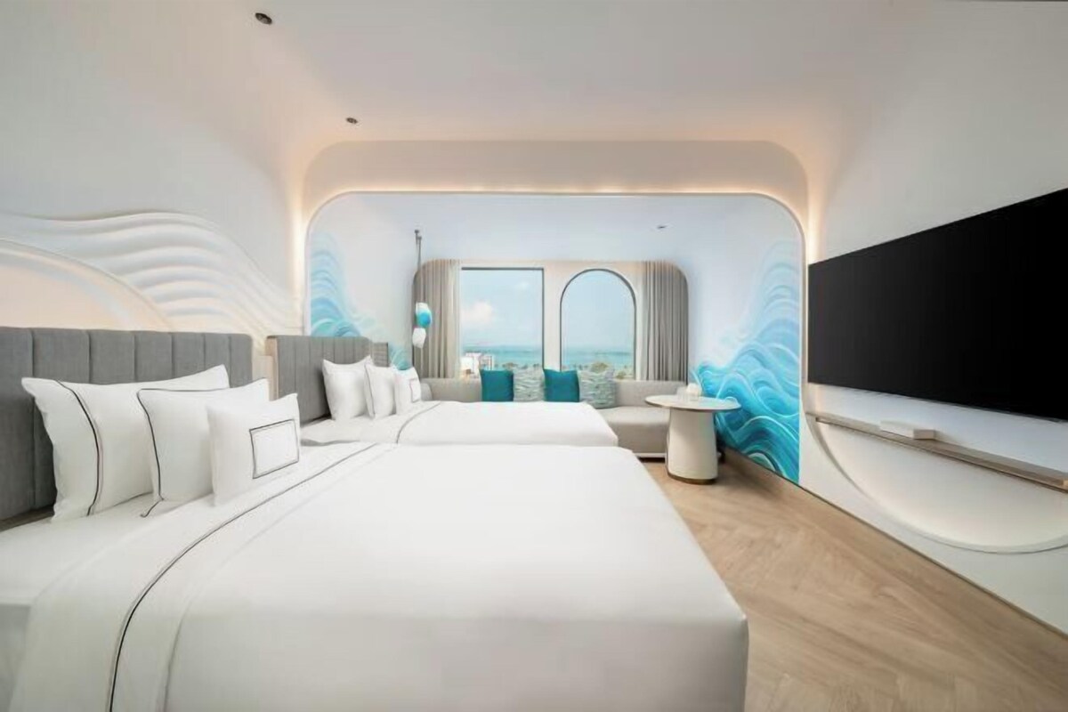 A modern hotel room with a large bed, a sofa, a TV, and a view of the ocean.