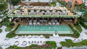 Ein Poolbereich auf dem Dach mit Liegestühlen und Sonnenschirmen, umgeben von Pflanzen und einer Bar.
