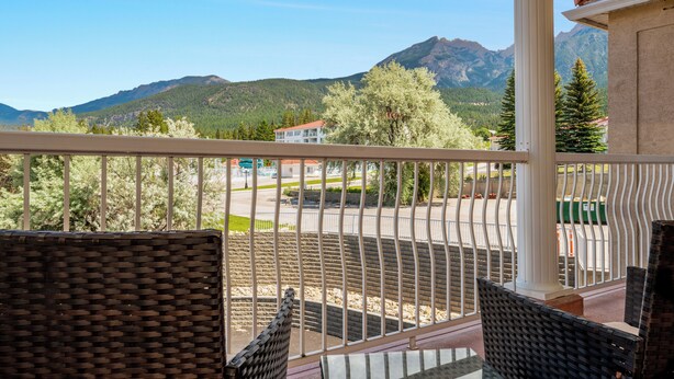 A balcony with wicker furniture, a view of a mountain range, and a building with a red roof in the background.
