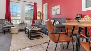 A modern living room with a red accent wall, a grey sofa, a coffee table, and a dining area with a round table and chairs.