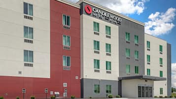 Un moderno edificio de hotel con un llamativo letrero de 'Candlewood Suites', varias ventanas y un estacionamiento.