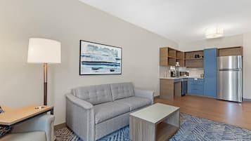 Una sala moderna con sofá, una mesa de centro y una zona de cocina con refrigerador, microondas y armarios.