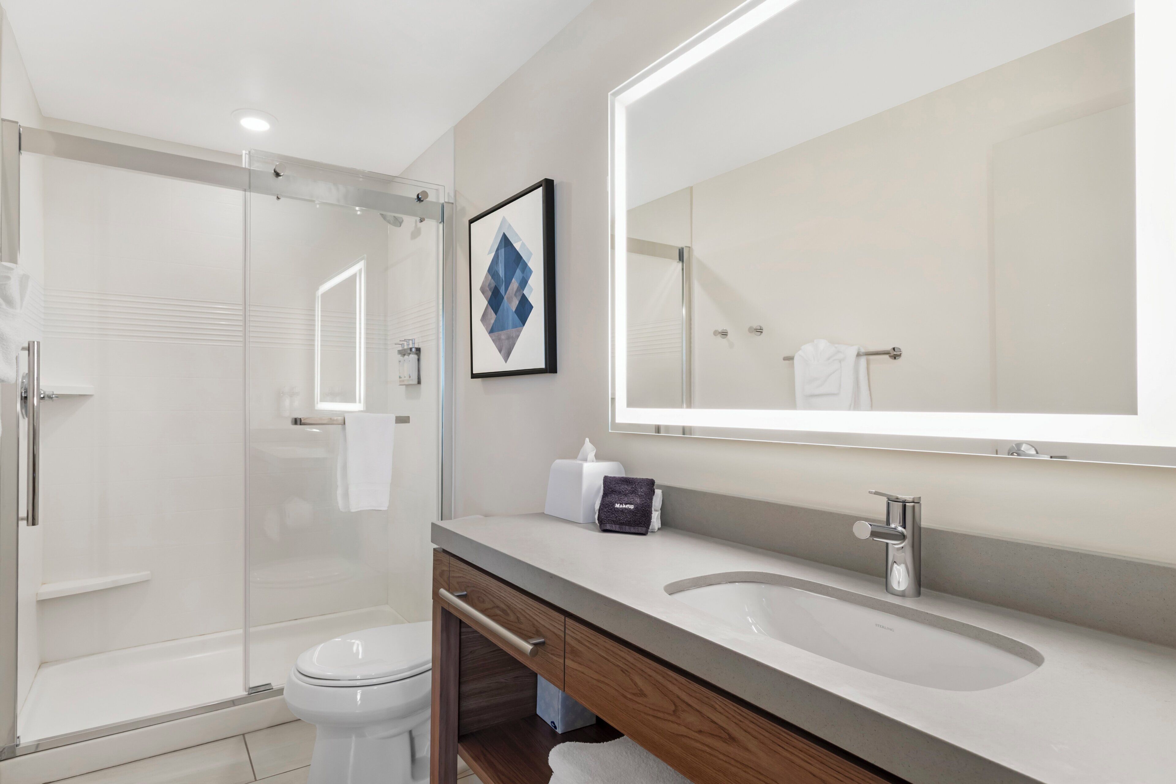 Un baño moderno con cabina de ducha de vidrio, inodoro blanco, tocador con espejo y lavamanos.