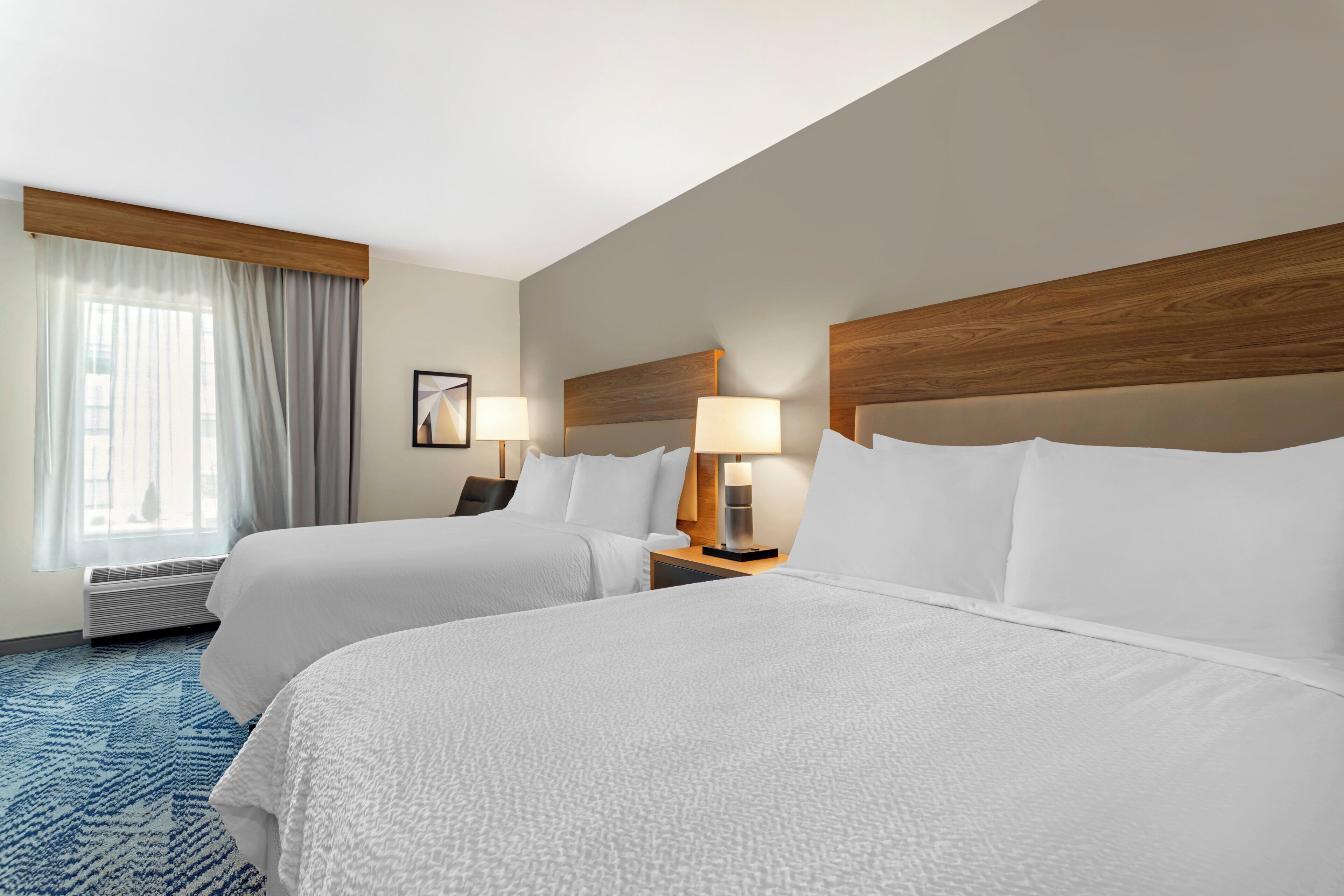 A hotel room with two beds, a window with curtains, a wall-mounted lamp, and a framed picture.