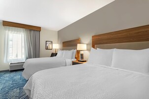 A hotel room with two beds, a window with curtains, a wall-mounted lamp, and a framed picture.
