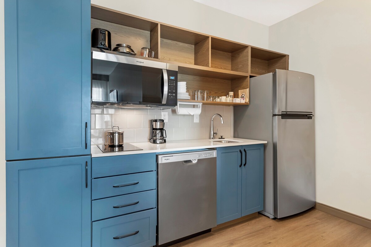 A modern kitchen with blue cabinets, a stainless steel refrigerator, a microwave, and a coffee maker.