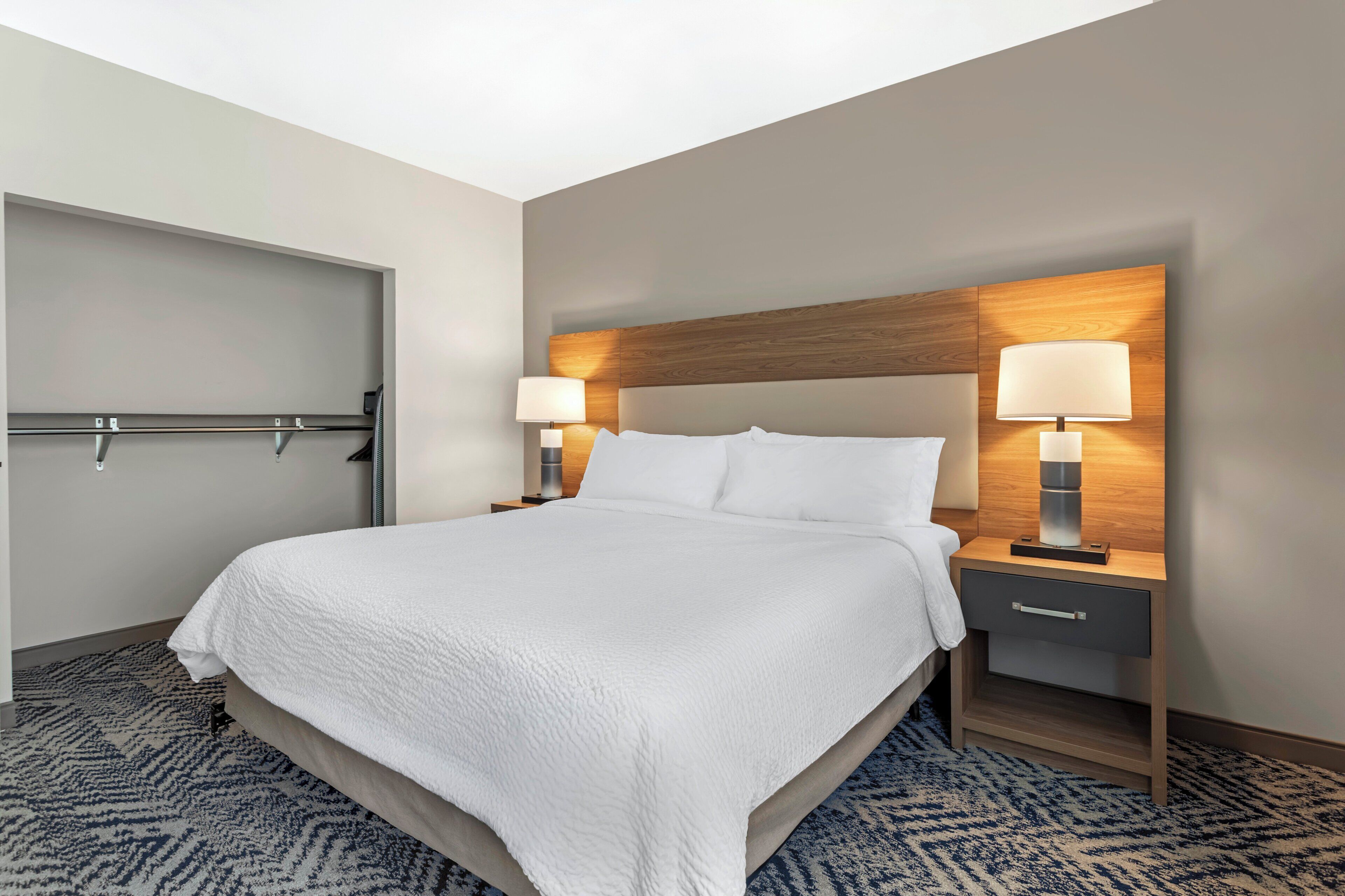 A hotel room with a bed, two bedside tables with lamps, a door, and a patterned carpet.