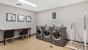 A laundry room with three stacked washing machines, a table with chairs, and a wall-mounted drying rack. - Candlewood Suites Morristown West by IHG (Morristown)
