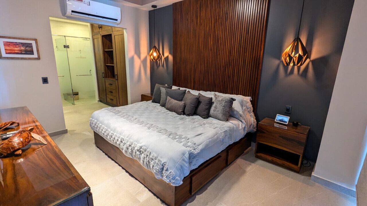 Une chambre à coucher avec un grand lit, une tête de lit en bois, des tables de chevet et un appareil de climatisation.
