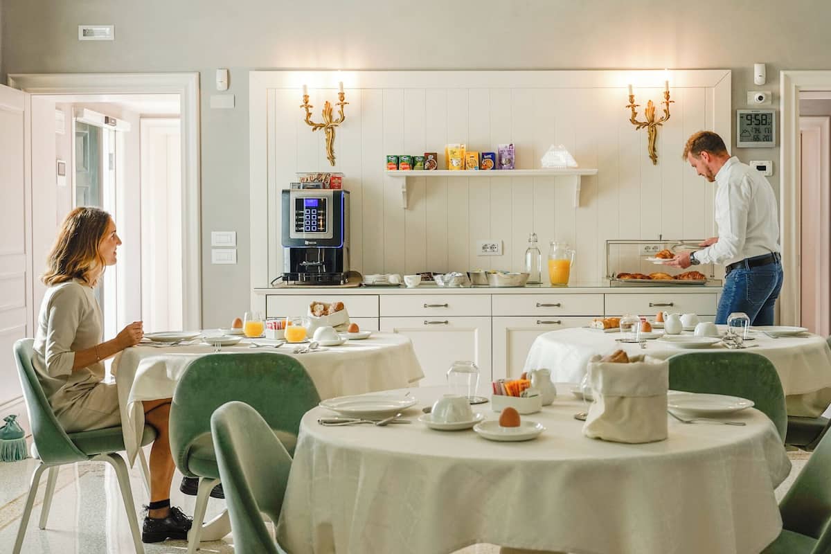 A breakfast setting with two tables, one with a person seated and another with a person serving food.