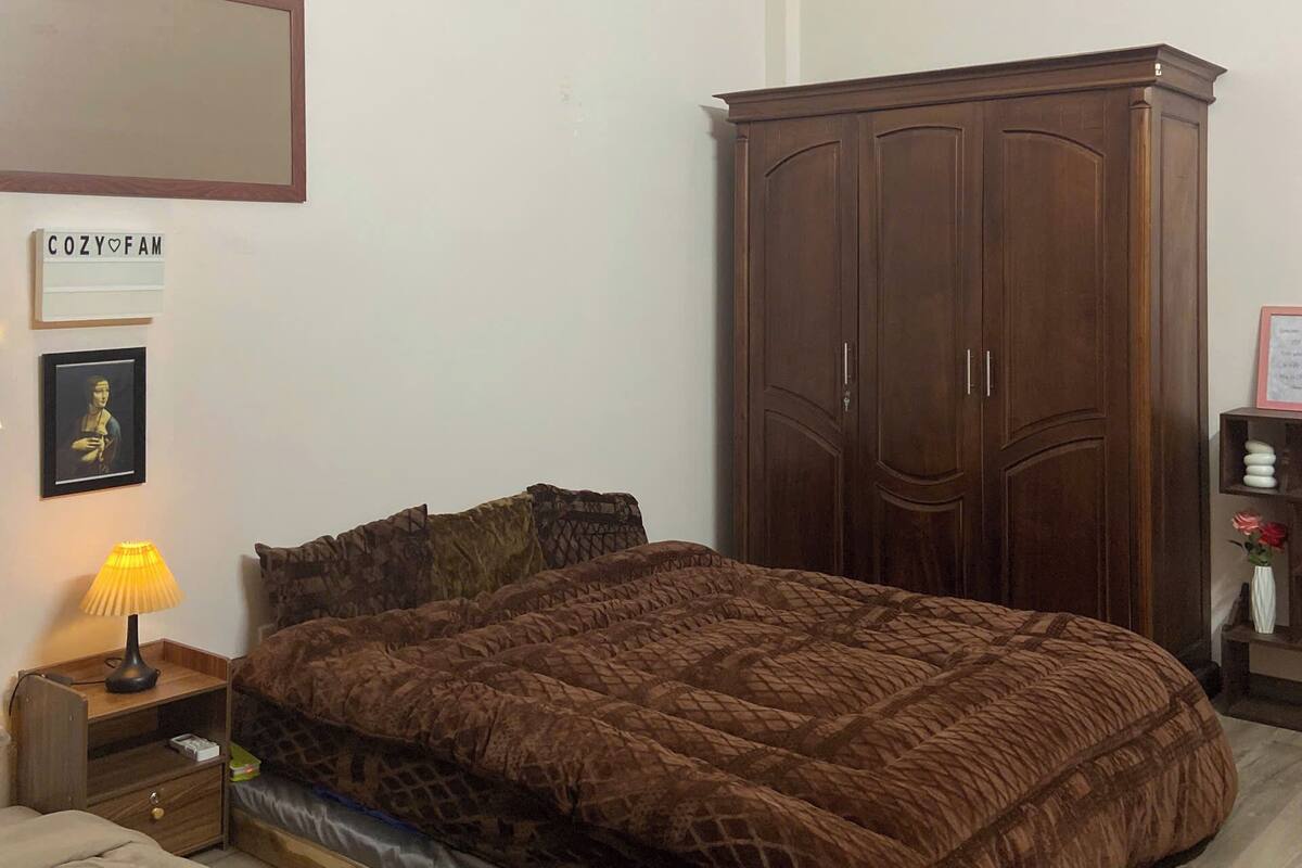 Un dormitorio con una cama, un armario de madera, una mesita de noche con una lámpara, un cuadro enmarcado y un cartel en la pared.