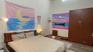 Una camera da letto con un letto grande, un armadio in legno, un comodino con una lampada e un arazzo raffigurante un tramonto sull'acqua.