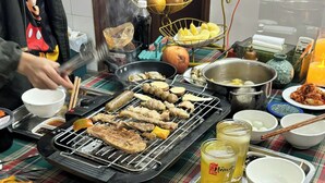 Un tavolo con diversi cibi, tra cui carni alla griglia e salsicce, e una persona che cucina alla griglia.