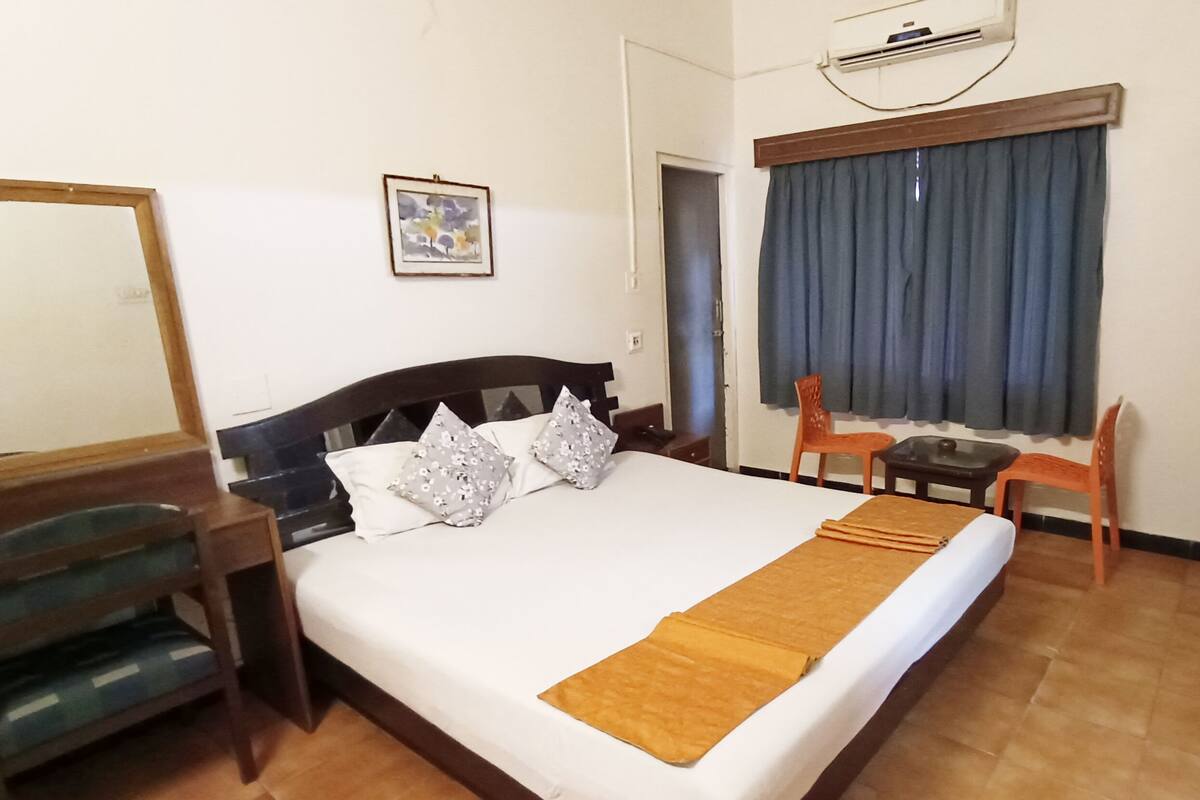 A hotel room with a bed, a desk, a chair, a small table, and a window with curtains.