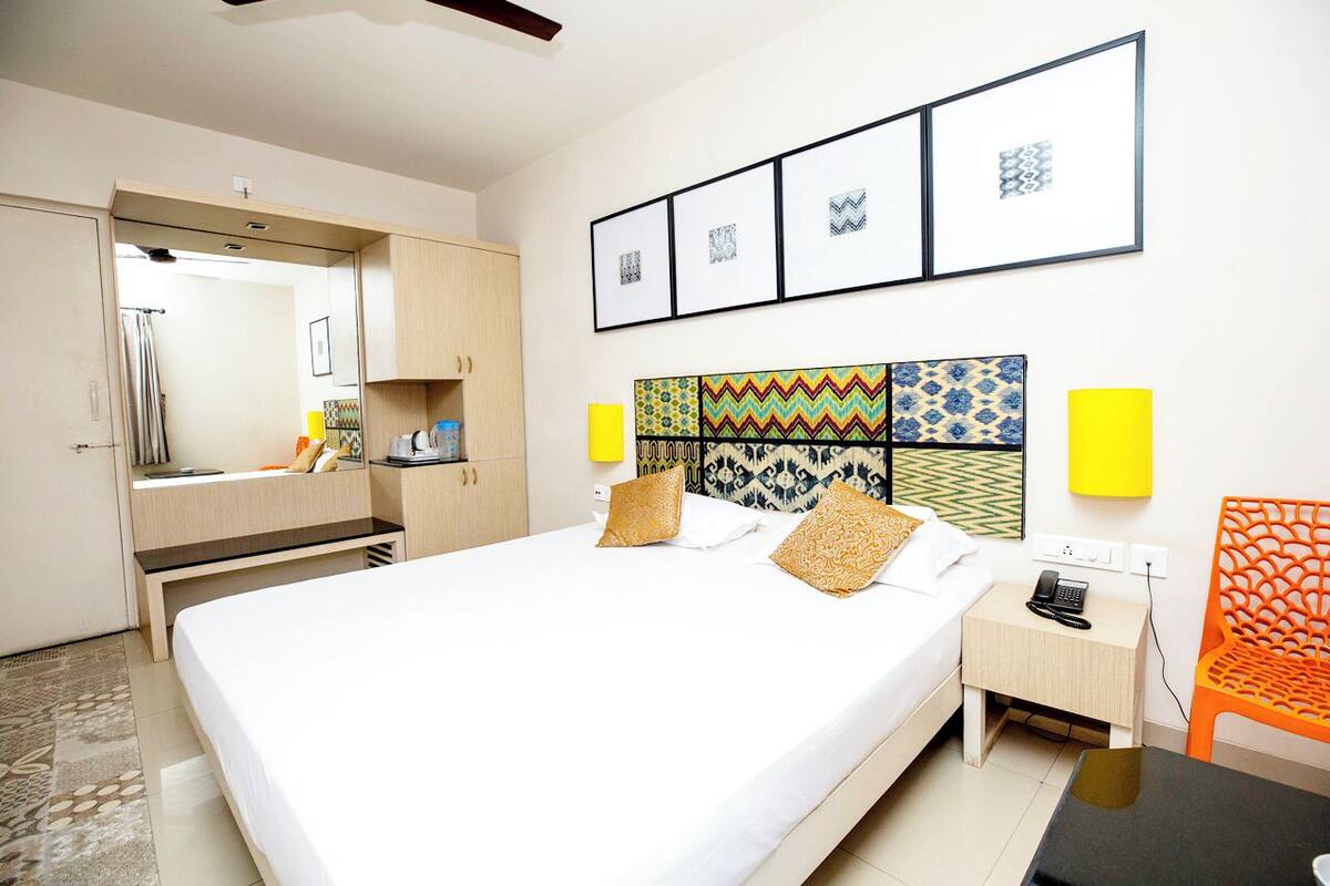 A hotel room with a large bed, a bedside table with a phone, a chair, and a wardrobe.