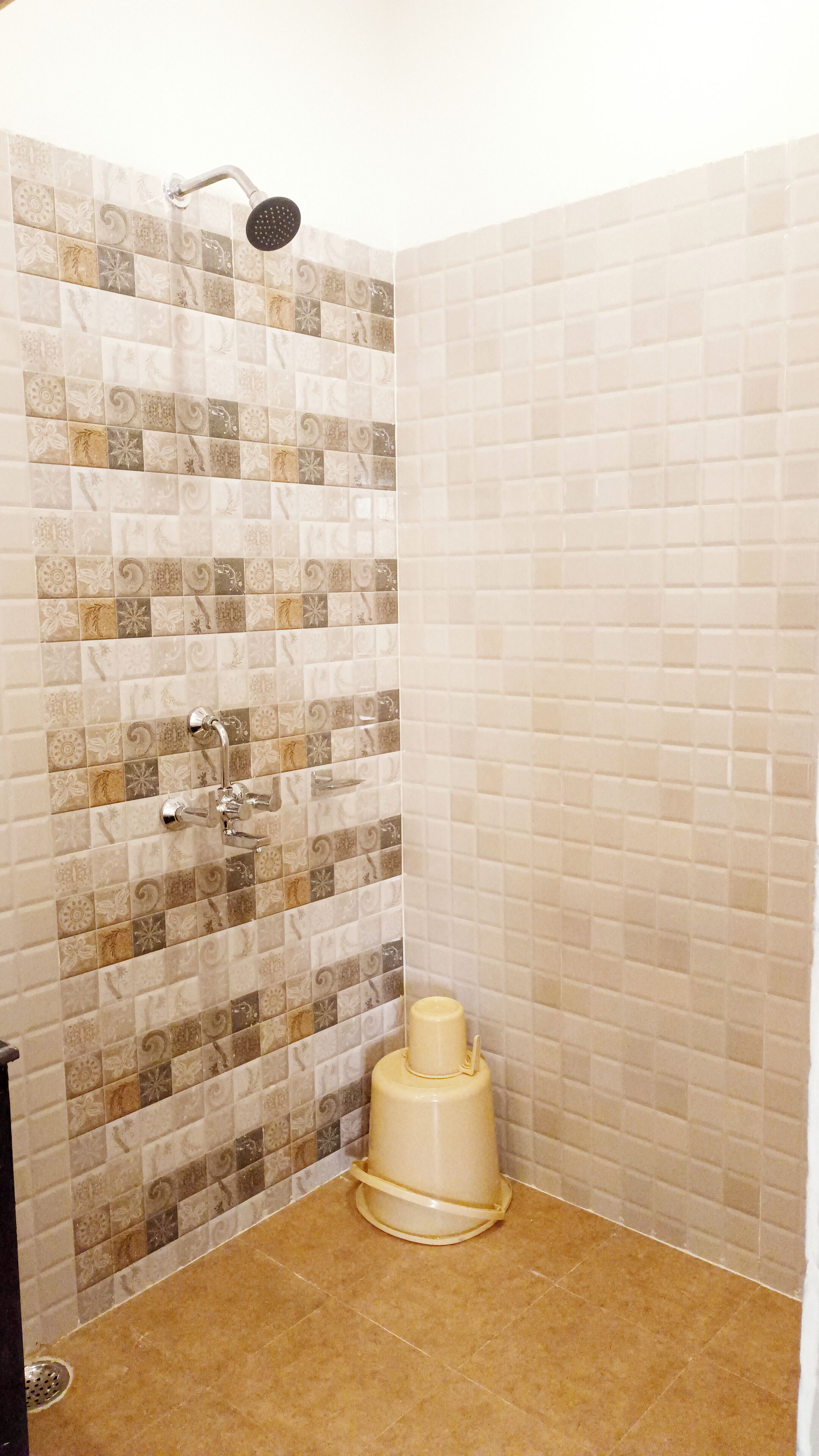En bruser med brusehoved i taghøjde og håndbruser, et beige toilet og et flisegulv.