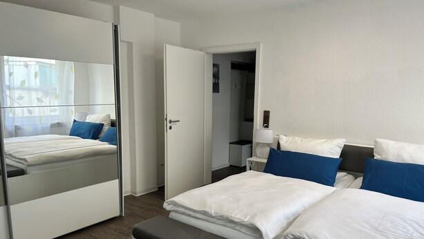 A modern bedroom with a large mirror, a bed with white and blue bedding, a bedside table with a lamp, and a wardrobe. - Melanie vacation apartment near Bad Ems thermal baths (Bad Ems)