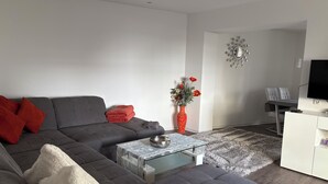A modern living room with a grey sofa, red cushions, a glass coffee table, a white cabinet, and a TV on a stand. - Melanie vacation apartment near Bad Ems thermal baths (Bad Ems)