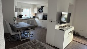 A modern kitchen with white cabinets, a dining area with a table and chairs, and a TV on a white stand. - Melanie vacation apartment near Bad Ems thermal baths (Bad Ems)