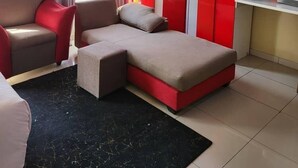 A modern room with a sofa, a desk with a TV, and a red cabinet. - AT BLACK WOOD GUEST HOUSE  (Pretoria)