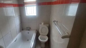 A bathroom with a bathtub, toilet, and a window providing natural light. - AT BLACK WOOD GUEST HOUSE  (Pretoria)