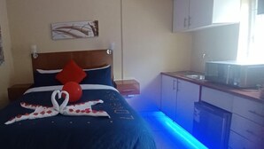 A hotel room with a bed, a nightstand, a small table, a microwave, and cabinets. - AT BLACK WOOD GUEST HOUSE  (Pretoria)