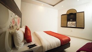 A modern hotel room with a bed, pillows, a blanket, a wall-mounted TV, and a decorative wall piece. - Hotel Sunrise DX (New Delhi)