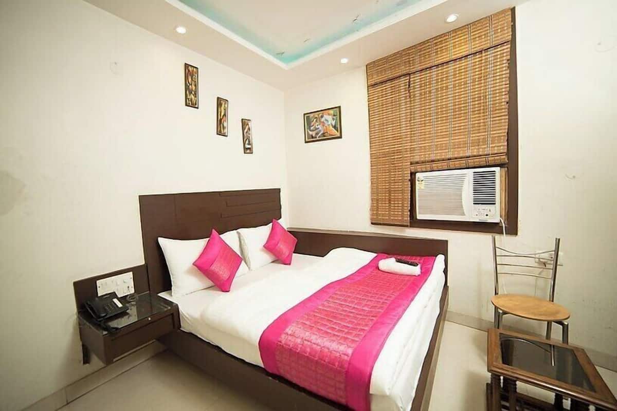 A hotel room with a bed, bedside table, chair, and artwork on the walls.