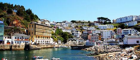 A coastal town with buildings along the waterfront, boats docked near the shore, and a rocky breakwater.