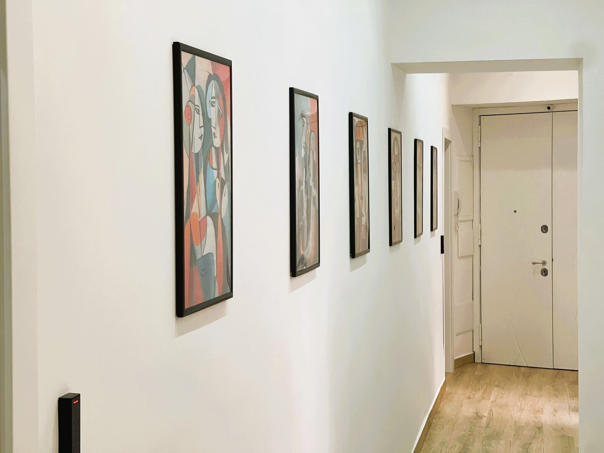 A hallway with a series of framed artworks on the wall and a door at the end.