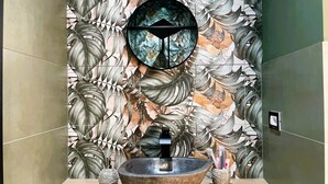 Un bagno con lavabo in pietra, uno specchio fissato alla parete e una parete decorata con motivi a foglia.