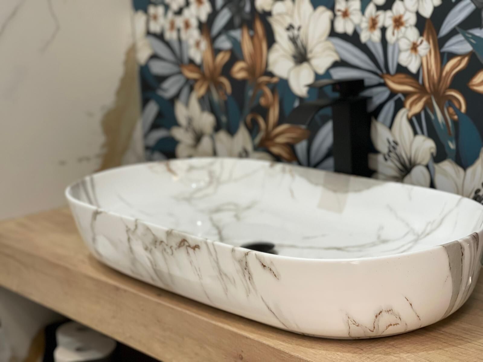 A white marble sink with a floral wallpaper background.