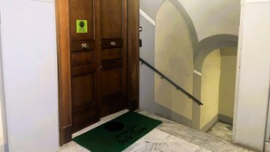 Una porta doppia in legno all'ingresso, con un tappetino verde, che dà su una scalinata con corrimano.