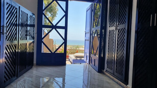 Blick durch ein Metallgitter zu einem Balkon mit Fliesenboden und einem Bett.