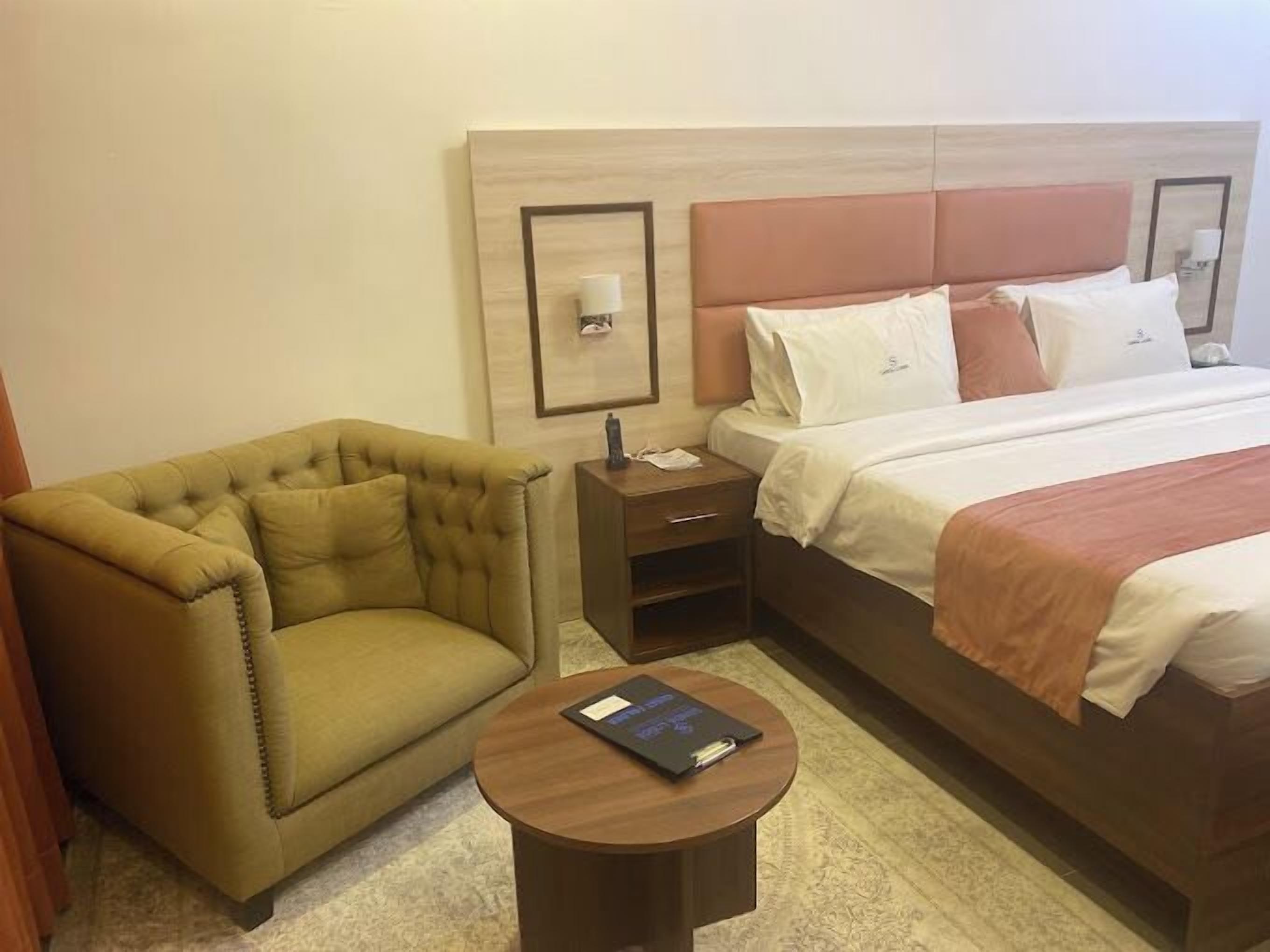 A hotel room with a bed, a sofa, a bedside table, and a small round table with a book.