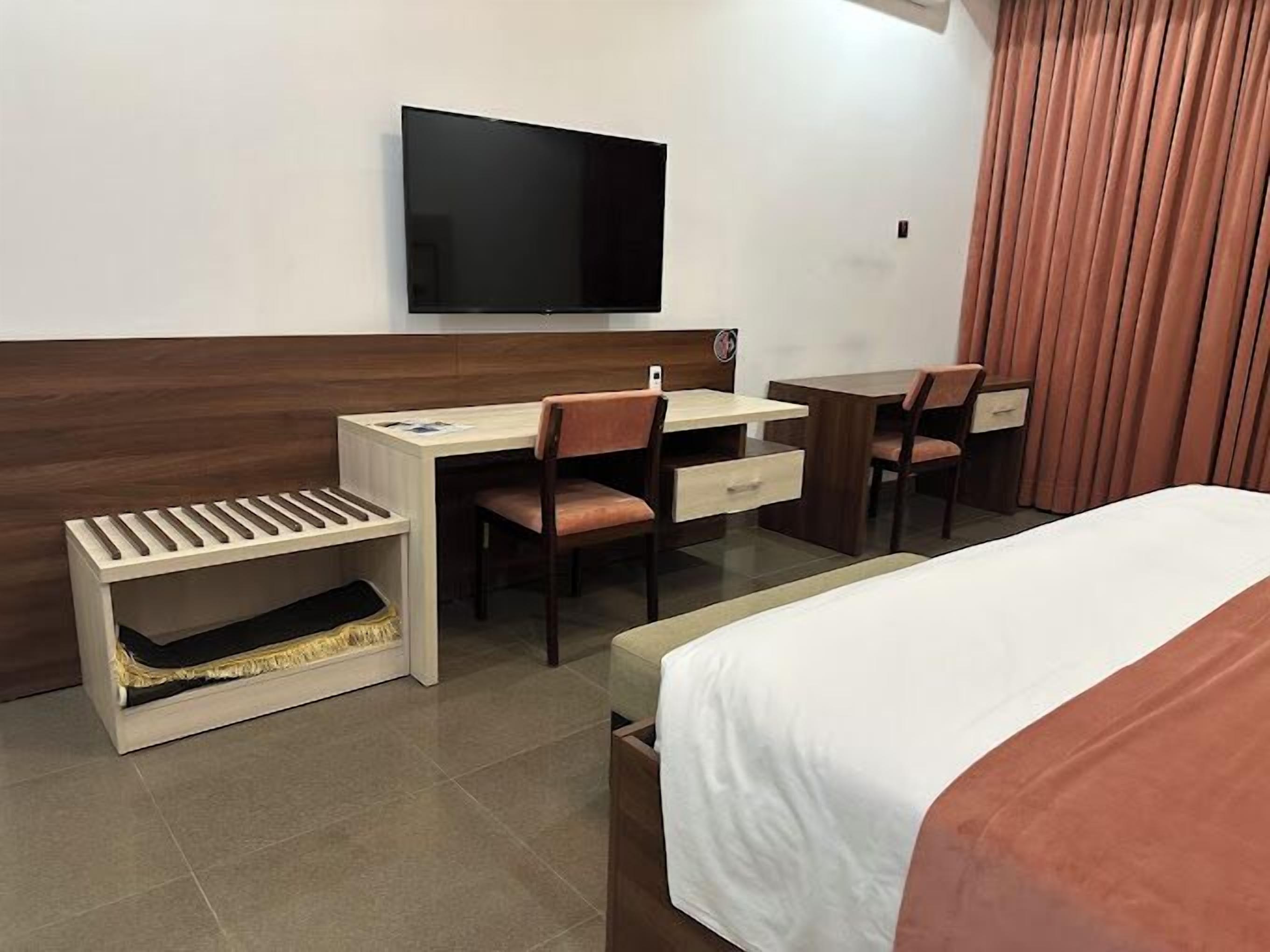 A hotel room with a bed, a desk with a chair, a television, and a window with curtains.