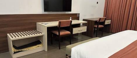 A hotel room with a bed, a desk with a chair, a television, and a window with curtains.