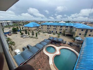 A view of a building with multiple floors, a swimming pool, and covered outdoor seating areas. - Ayalla Hotels Limited (Yenagoa)