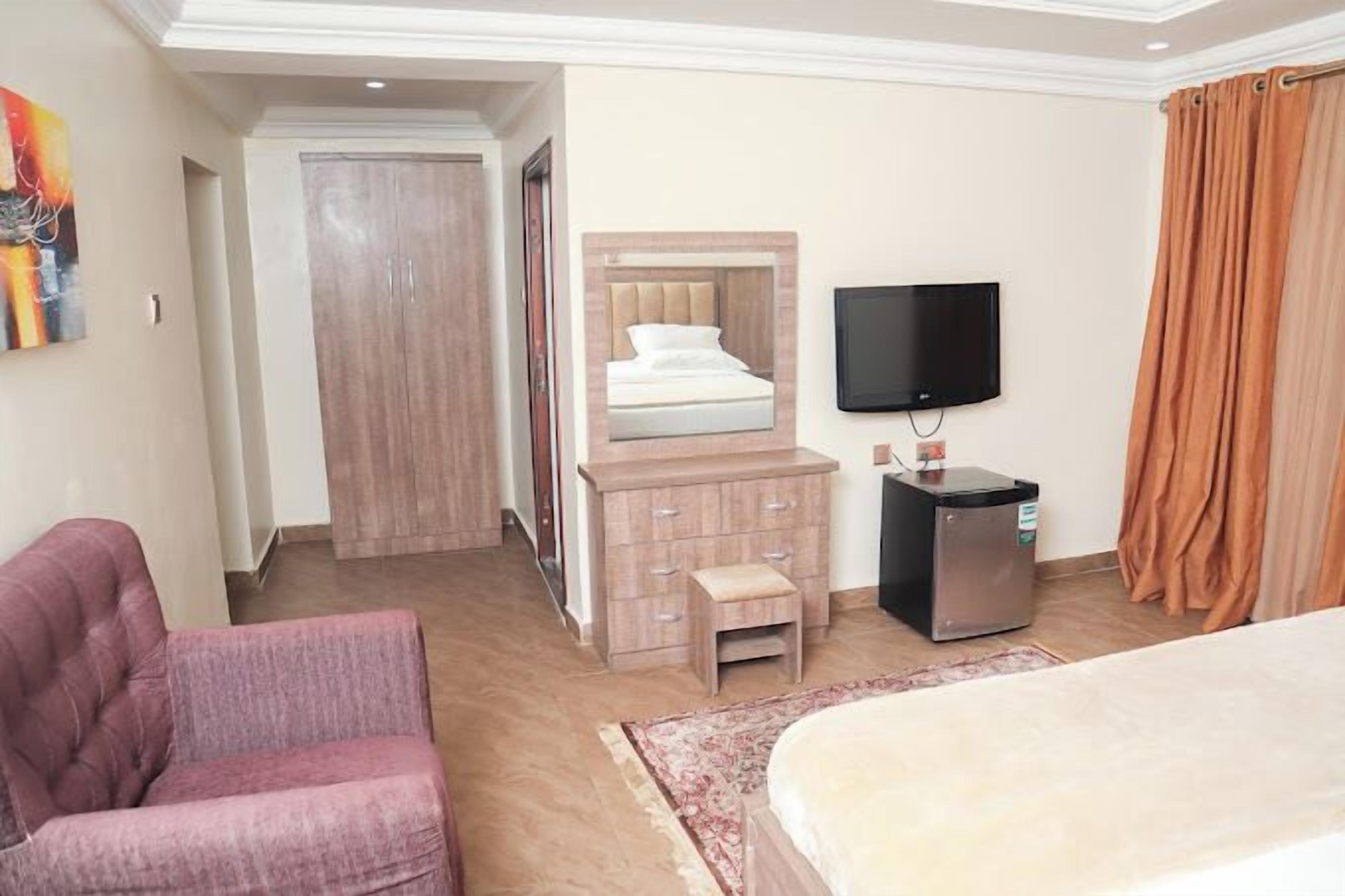 Una camera d'albergo con un letto, una televisione, un minibar, un tavolino, una sedia e un armadio.