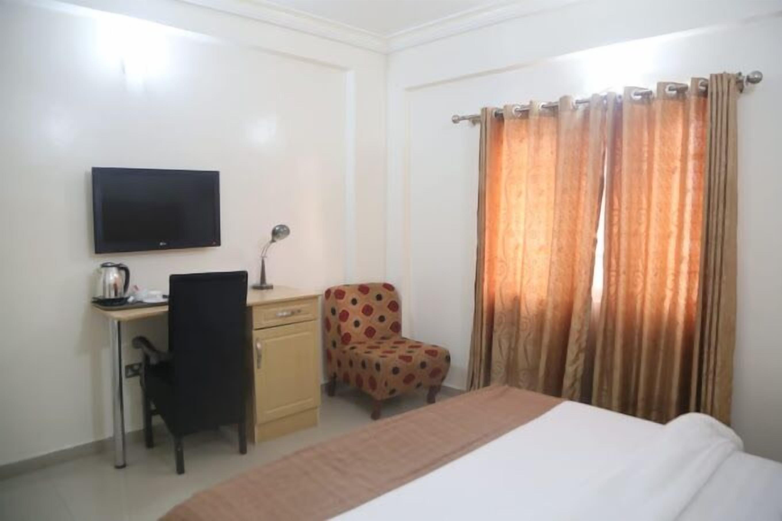 A hotel room with a bed, a desk with a chair, a television, and curtains.