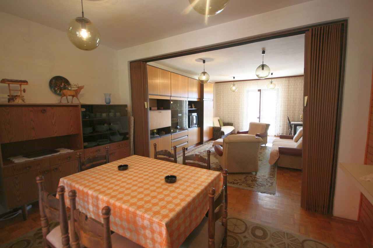 Ein Essbereich mit Tisch für zwei, eine Küche im Hintergrund und ein Wohnzimmer mit Sofa und Fernseher.