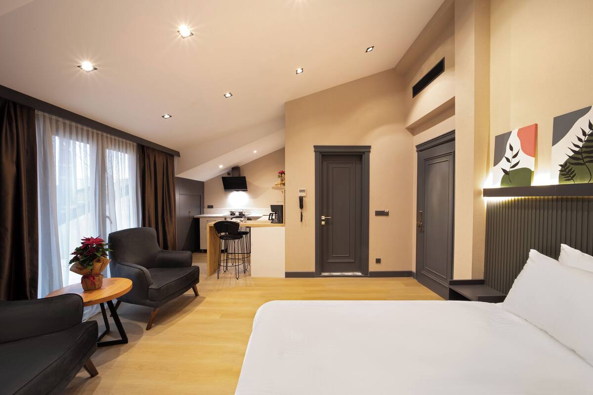 A hotel room with a large bed, a desk, a chair, and a small table with a plant.