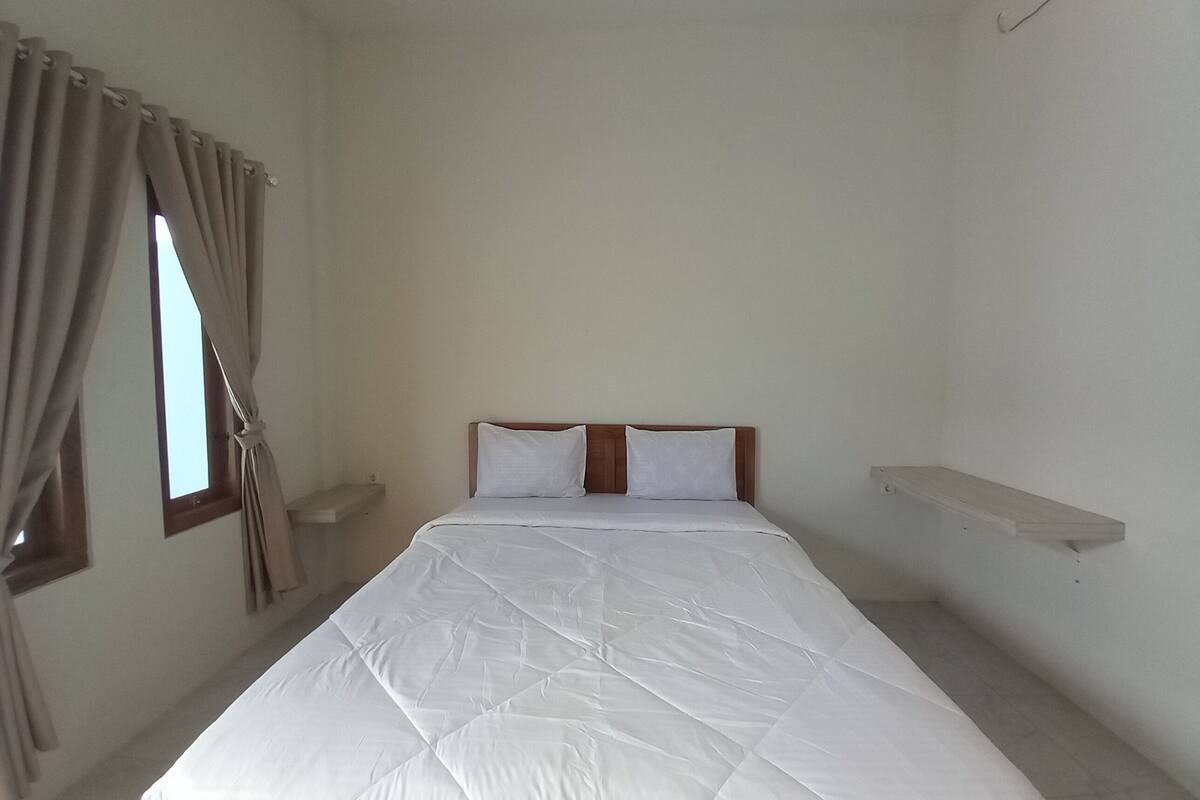 A simple, clean room with a bed, curtains, a window, and a shelf.